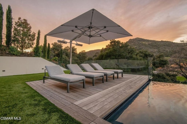 deck at dusk featuring a mountain view and a lawn