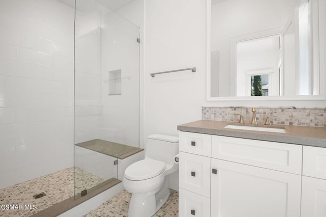 bathroom featuring a tile shower, vanity, toilet, and backsplash