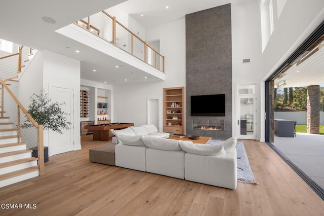 living room with built in shelves, a high ceiling, light hardwood / wood-style flooring, a fireplace, and pool table