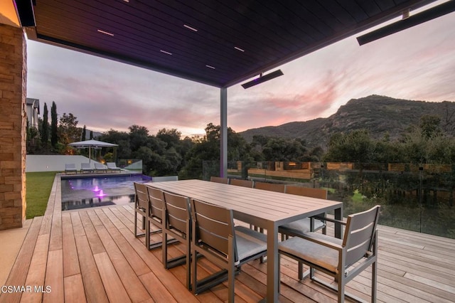 deck at dusk with a fenced in pool and a mountain view