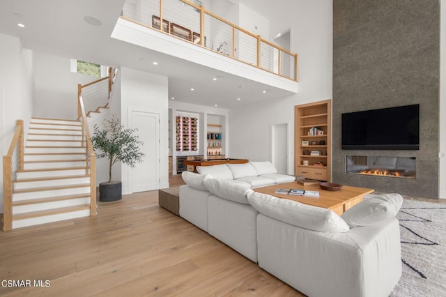 living room featuring built in features, a large fireplace, a high ceiling, and light wood-type flooring