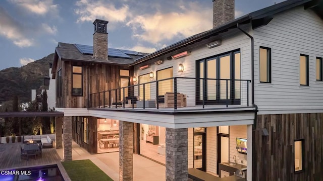 back house at dusk with solar panels, an outdoor hangout area, a balcony, a mountain view, and a patio