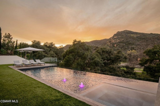 pool at dusk with a mountain view, a yard, and a patio