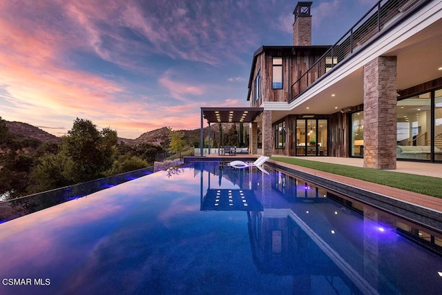 pool at dusk featuring a jacuzzi, a mountain view, and a patio