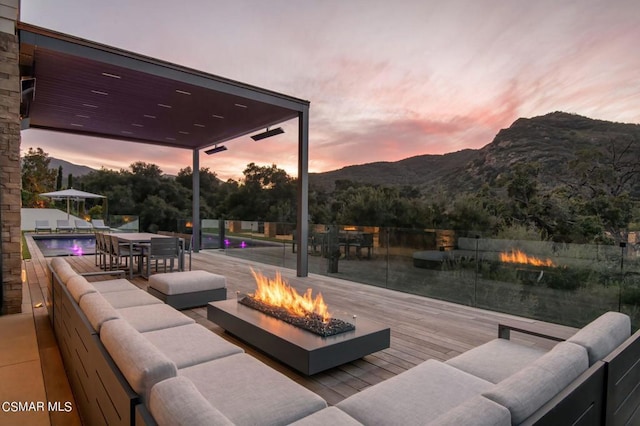 patio terrace at dusk with a deck with mountain view and an outdoor living space with a fire pit