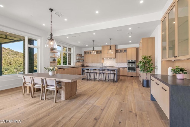 kitchen with a kitchen breakfast bar, tasteful backsplash, light hardwood / wood-style flooring, and hanging light fixtures