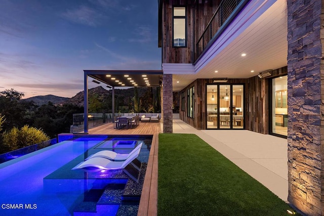 pool at dusk featuring a jacuzzi, a mountain view, a patio, and an outdoor hangout area