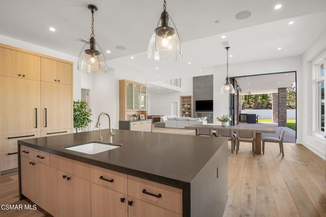 kitchen with sink, hanging light fixtures, a center island with sink, and light brown cabinets