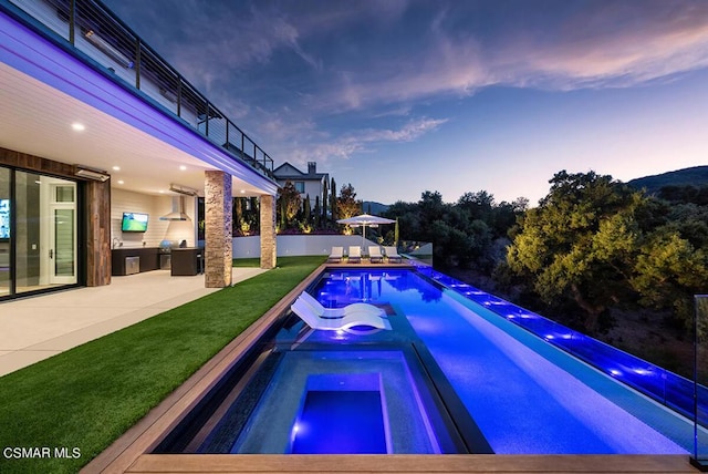 pool at dusk with an in ground hot tub, an outdoor kitchen, and a patio area