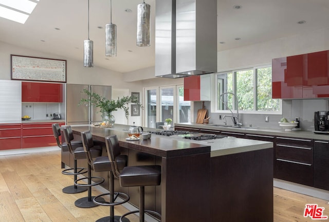 kitchen featuring sink, a kitchen island, stainless steel gas cooktop, light hardwood / wood-style floors, and vaulted ceiling with skylight