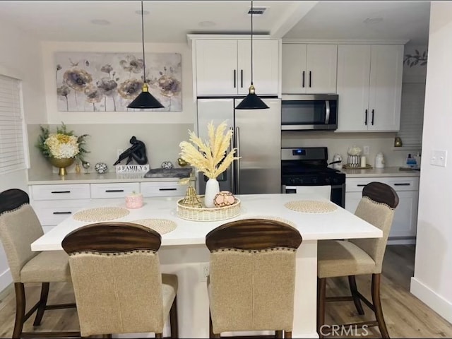 kitchen featuring light wood-type flooring, a breakfast bar, decorative light fixtures, stainless steel appliances, and white cabinets