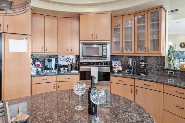 kitchen featuring dark stone countertops, appliances with stainless steel finishes, light brown cabinets, and decorative backsplash