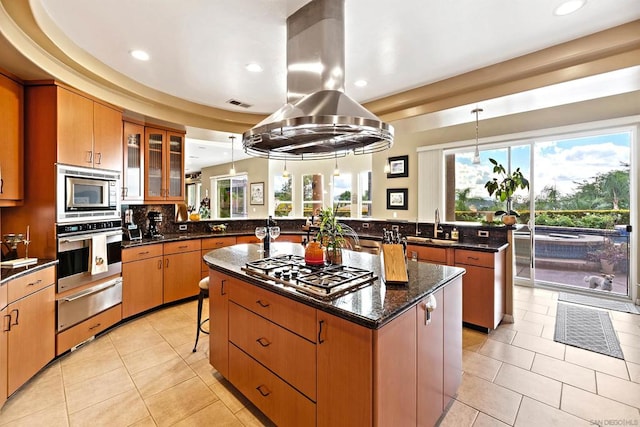 kitchen with appliances with stainless steel finishes, kitchen peninsula, hanging light fixtures, a breakfast bar area, and a center island with sink