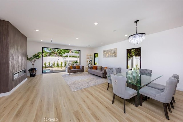 dining room with a chandelier, light wood-type flooring, and a large fireplace