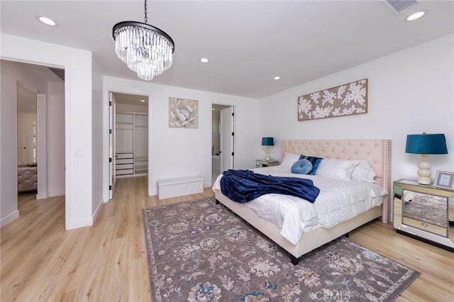 bedroom with a walk in closet, an inviting chandelier, light hardwood / wood-style flooring, and a closet