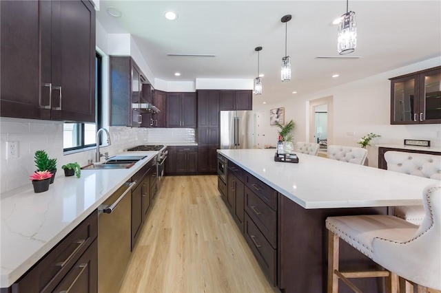 kitchen featuring a kitchen breakfast bar, premium appliances, sink, decorative light fixtures, and light hardwood / wood-style flooring