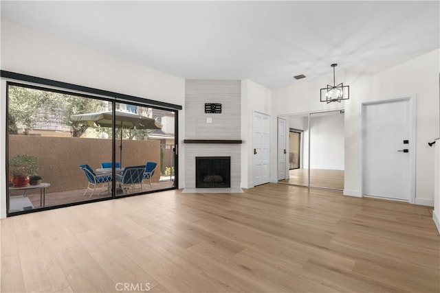 unfurnished living room with an inviting chandelier, a fireplace, and light hardwood / wood-style floors