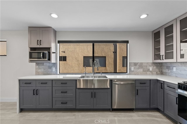 kitchen with tasteful backsplash, light wood-type flooring, sink, gray cabinets, and stainless steel appliances