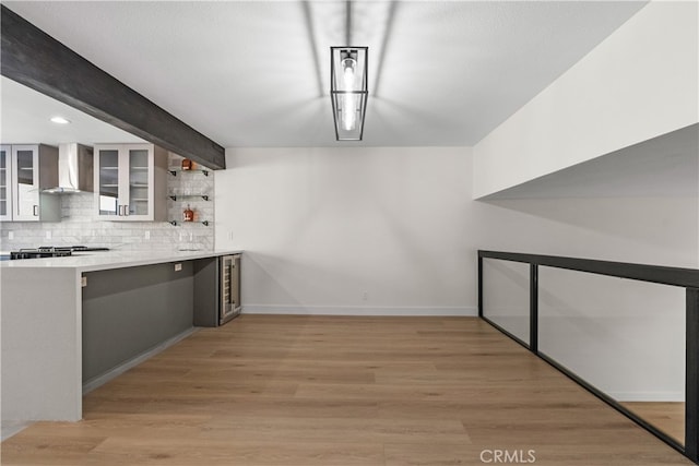 interior space featuring white cabinets, backsplash, light wood-type flooring, beamed ceiling, and wall chimney exhaust hood