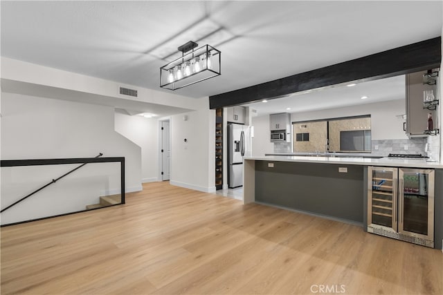 kitchen with decorative backsplash, beamed ceiling, light wood-type flooring, beverage cooler, and appliances with stainless steel finishes