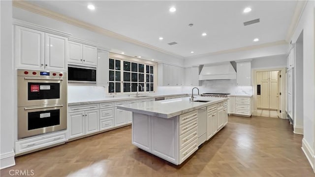 kitchen featuring light parquet flooring, premium range hood, white cabinetry, a kitchen island with sink, and double oven