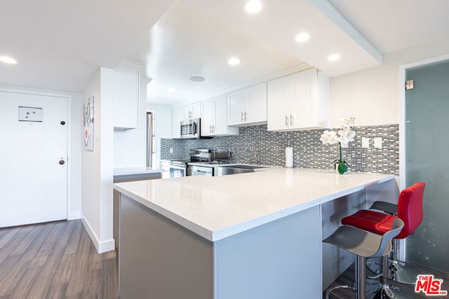 kitchen featuring white cabinets, appliances with stainless steel finishes, kitchen peninsula, light stone counters, and a breakfast bar