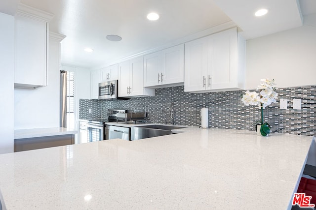 kitchen featuring kitchen peninsula, stainless steel appliances, light stone countertops, white cabinets, and sink