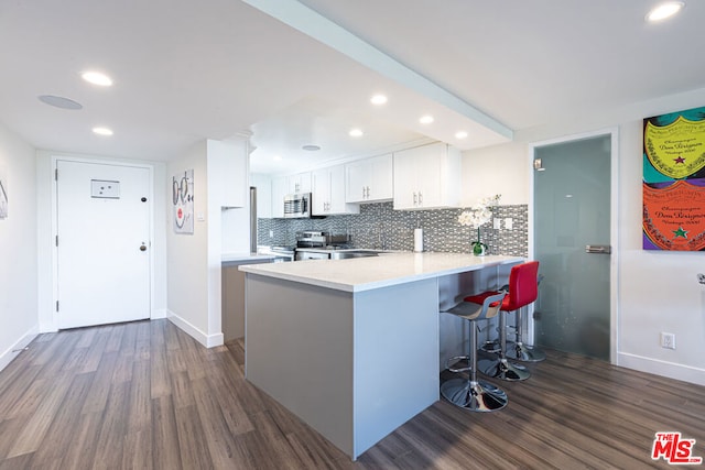 kitchen with white cabinets, stainless steel appliances, dark hardwood / wood-style floors, kitchen peninsula, and a breakfast bar