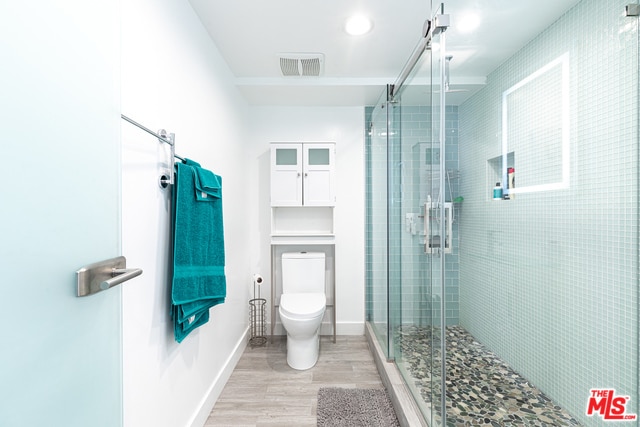 bathroom with toilet, hardwood / wood-style flooring, and an enclosed shower