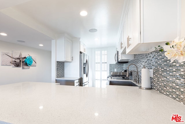 kitchen with tasteful backsplash, sink, white cabinetry, stainless steel fridge, and range