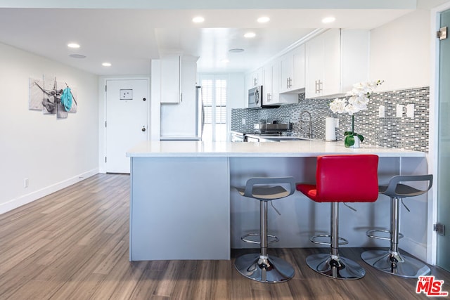 kitchen with dark wood-type flooring, white cabinets, kitchen peninsula, and a kitchen bar