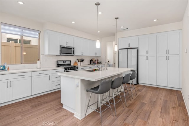 kitchen featuring pendant lighting, white cabinetry, a center island with sink, and appliances with stainless steel finishes