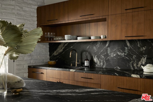 kitchen with brick wall, backsplash, sink, and dark stone countertops