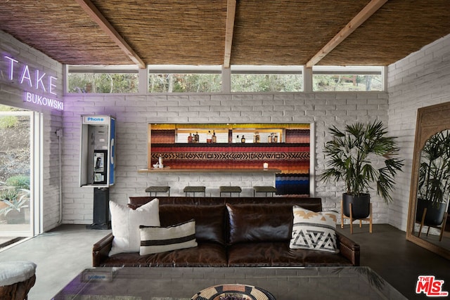 living room featuring beam ceiling, concrete floors, and brick wall