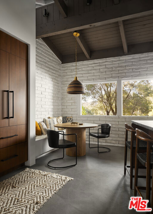 interior space with lofted ceiling with beams, brick wall, and concrete floors