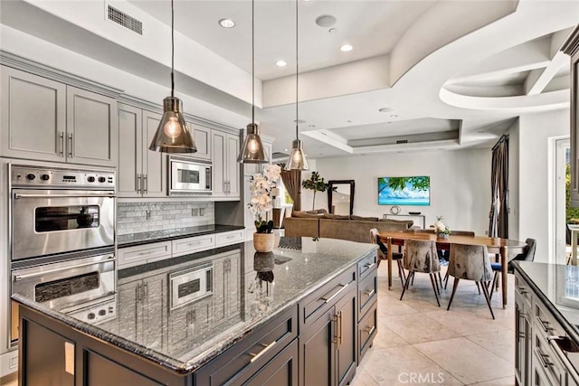 kitchen featuring dark stone counters, a raised ceiling, hanging light fixtures, light tile patterned floors, and stainless steel appliances