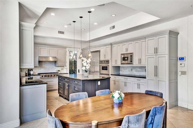 kitchen featuring appliances with stainless steel finishes, dark stone counters, gray cabinetry, pendant lighting, and a kitchen island