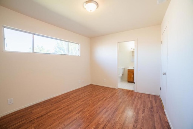 unfurnished bedroom with connected bathroom and hardwood / wood-style flooring