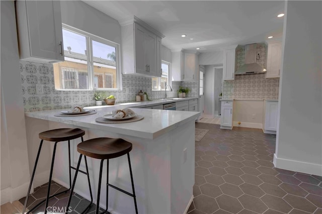 kitchen with wall chimney exhaust hood, white cabinets, kitchen peninsula, and tasteful backsplash