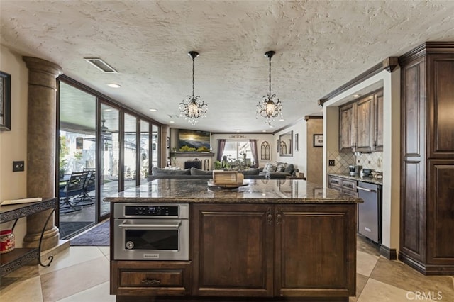 kitchen featuring backsplash, dark stone countertops, appliances with stainless steel finishes, dark brown cabinets, and a chandelier