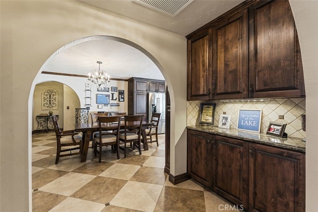 interior space featuring an inviting chandelier, decorative backsplash, high end refrigerator, decorative light fixtures, and dark stone counters