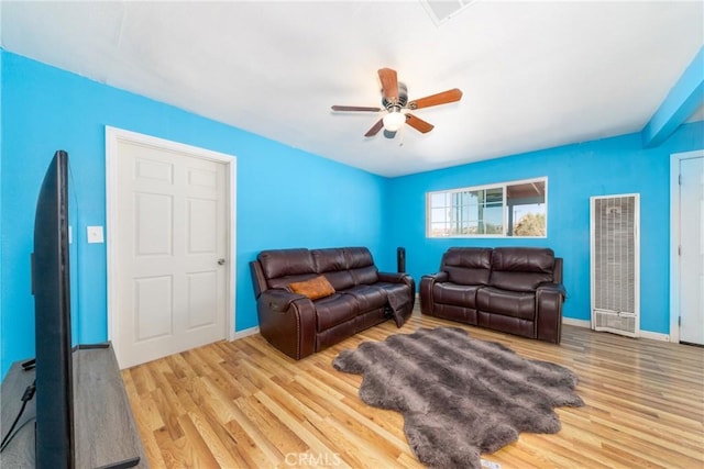 living area with baseboards, a ceiling fan, wood finished floors, and a heating unit