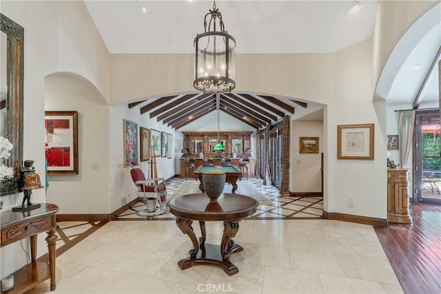 foyer featuring beam ceiling, high vaulted ceiling, arched walkways, baseboards, and a chandelier