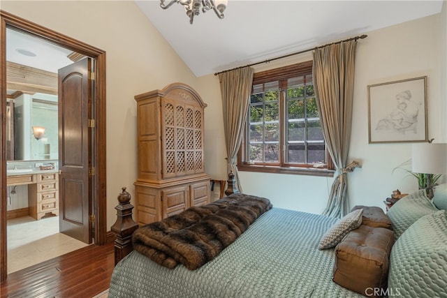 bedroom featuring an inviting chandelier, lofted ceiling, dark wood-type flooring, and connected bathroom