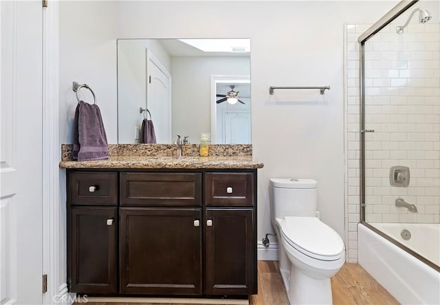 full bathroom featuring ceiling fan, wood-type flooring, toilet, shower / bath combination with glass door, and vanity