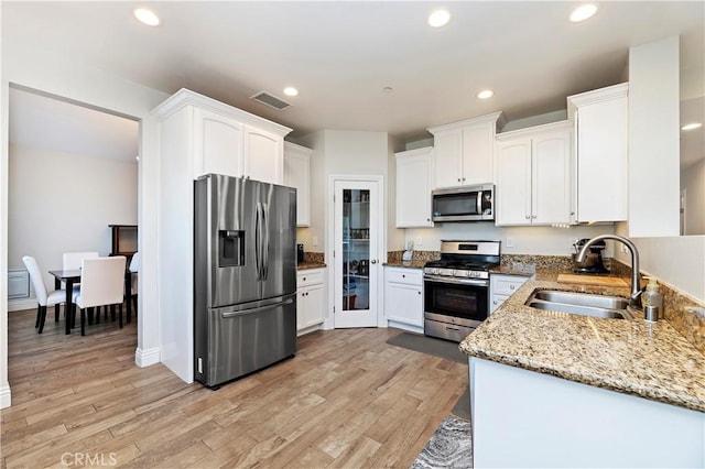 kitchen featuring light stone countertops, stainless steel appliances, sink, light hardwood / wood-style flooring, and white cabinets