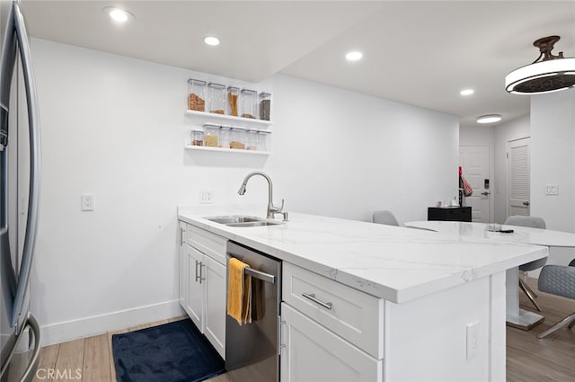 kitchen with appliances with stainless steel finishes, light hardwood / wood-style floors, white cabinetry, light stone counters, and sink