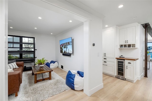 interior space featuring wine cooler, light wood-type flooring, recessed lighting, and crown molding