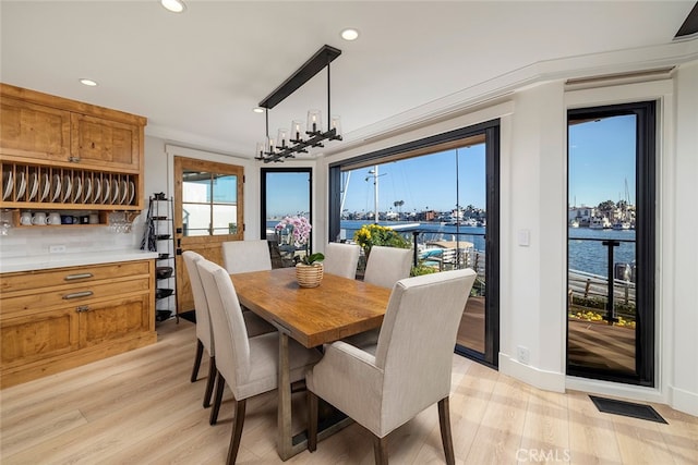 dining space with ornamental molding, a water view, light hardwood / wood-style floors, and a chandelier