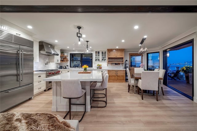 kitchen with open shelves, light countertops, wall chimney range hood, high quality appliances, and light wood-type flooring